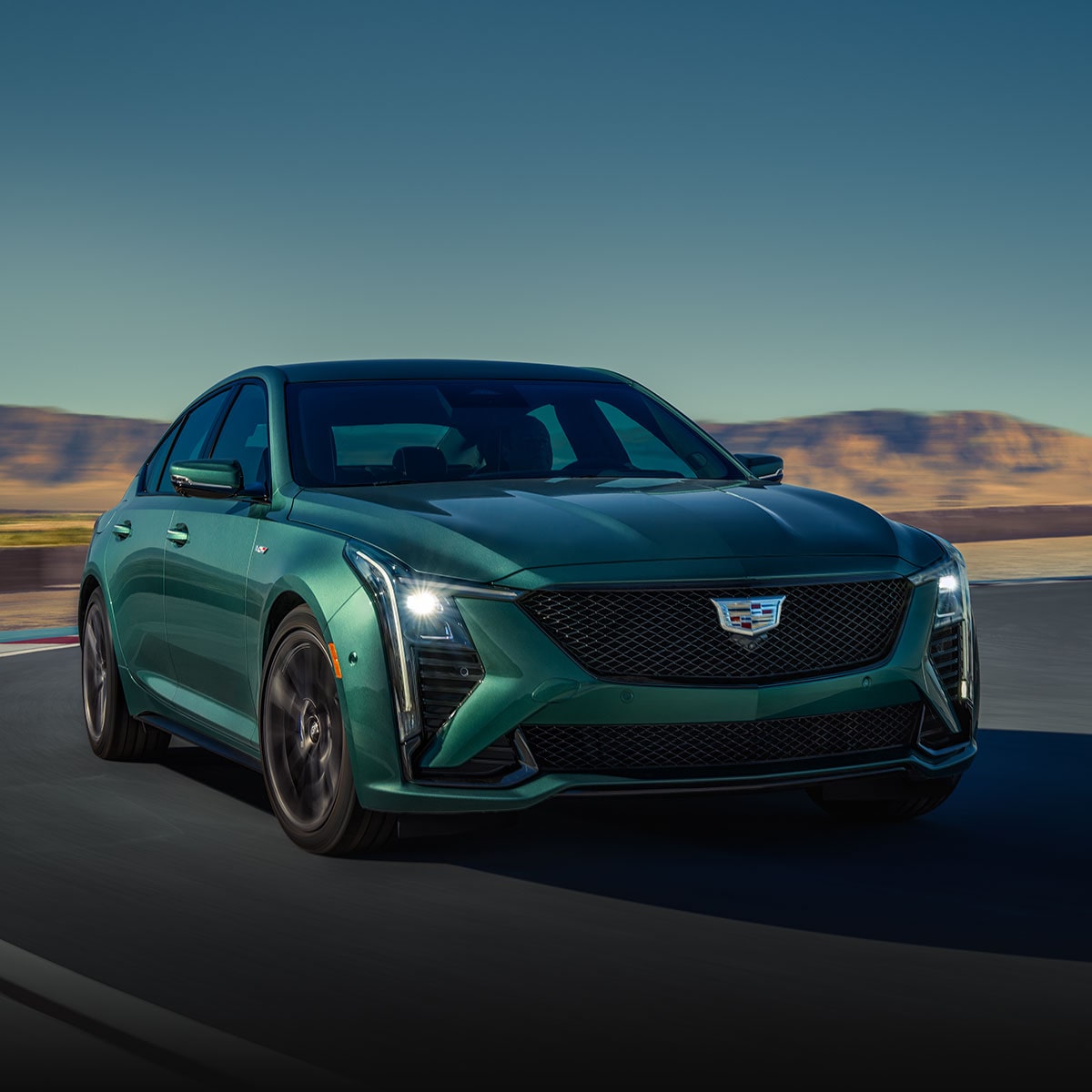 A Green Cadillac CT5-V Driving Down a Road with Mountains in the Background.